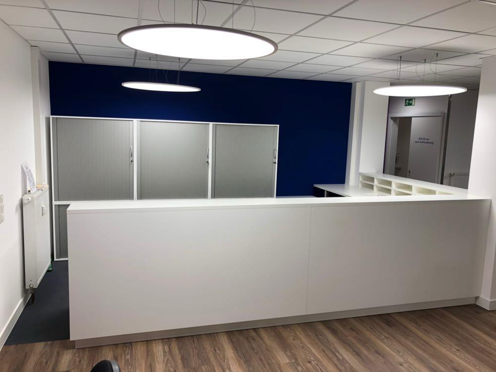 Leerer Empfangsbereich mit weißem Tresen, blauem Hintergrund und Holzboden