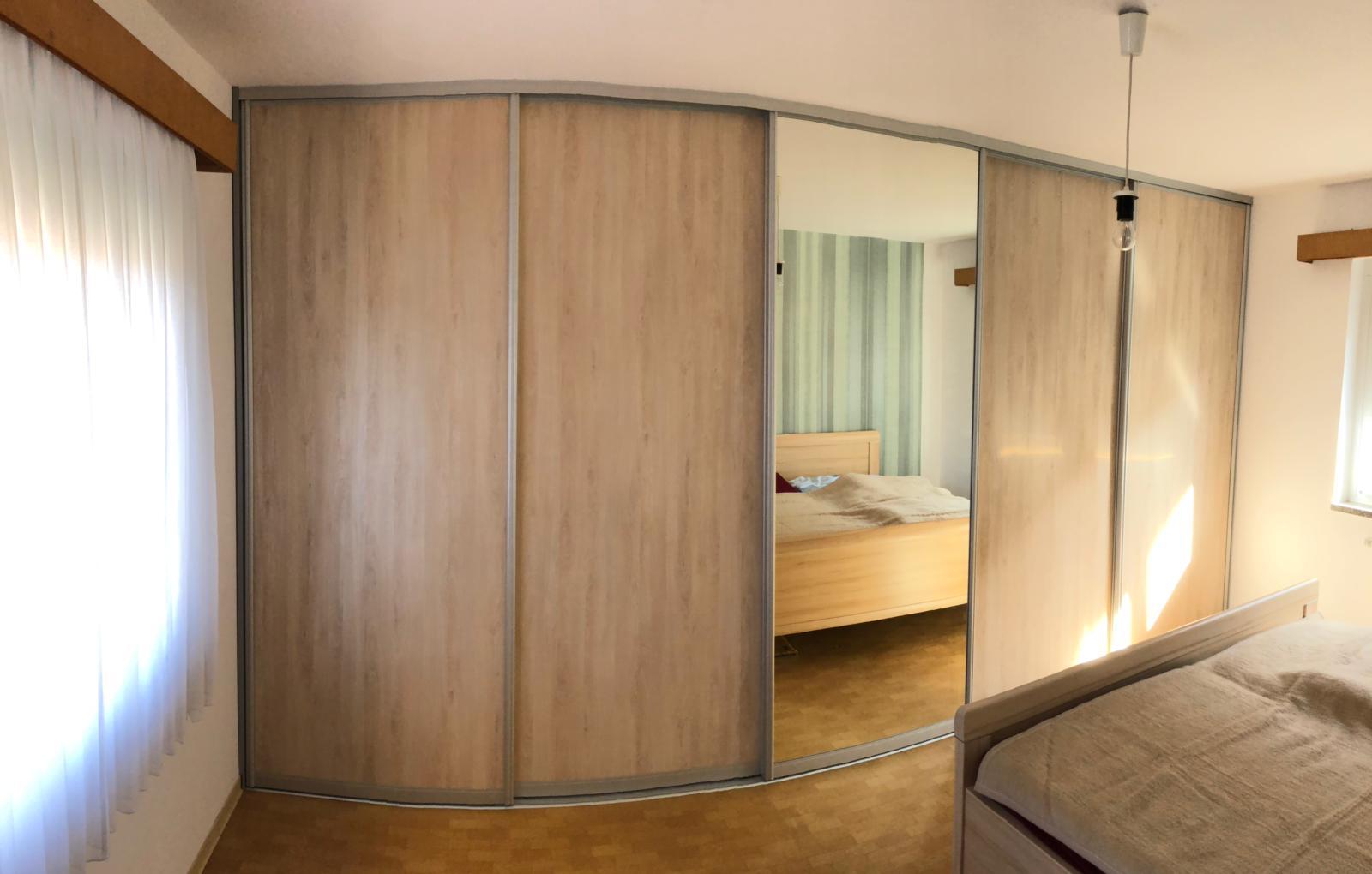 Helles Schlafzimmer mit großem Kleiderschrank mit Schiebetüren und Spiegel in der Mitte