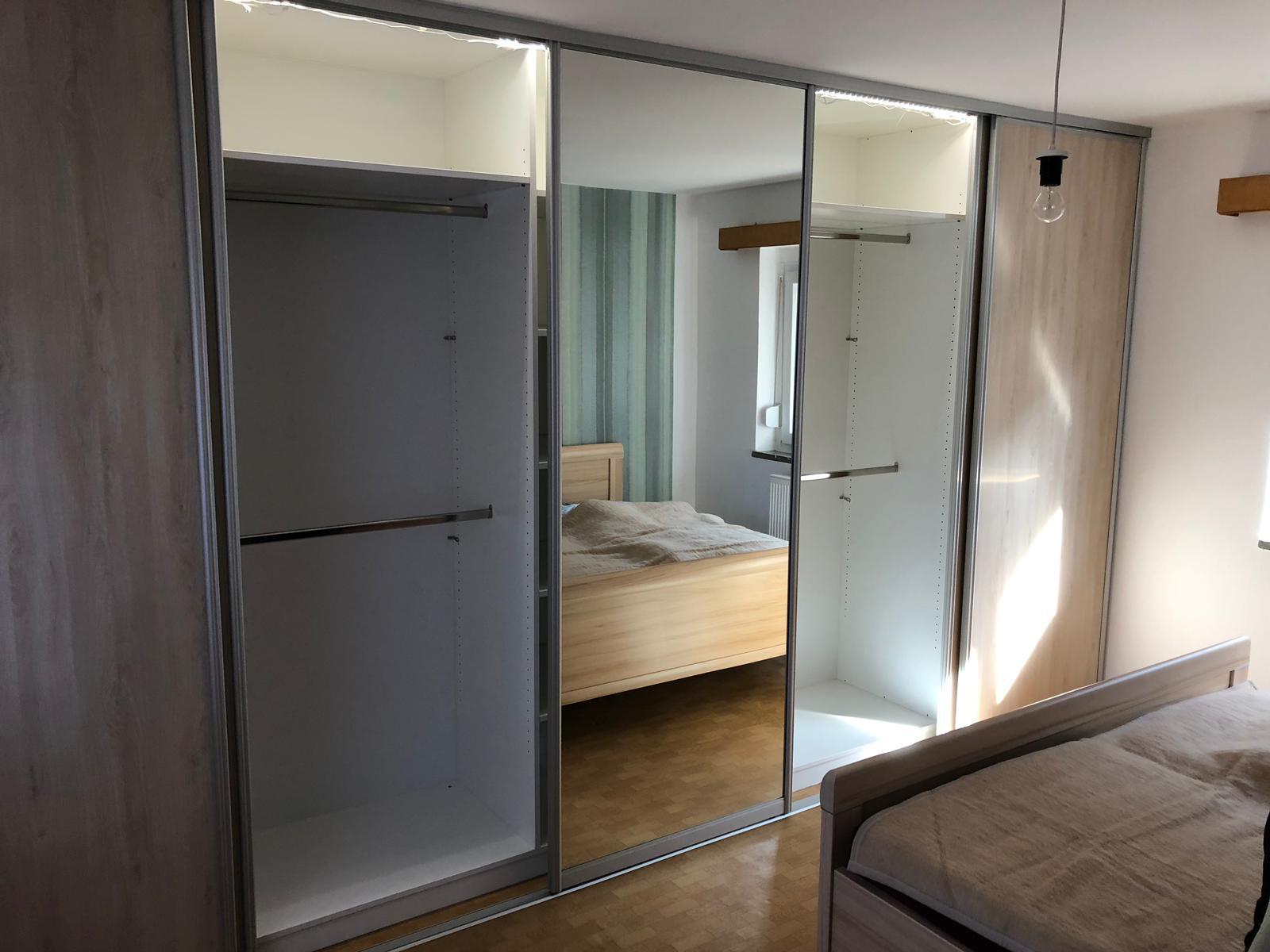 Ein Schlafzimmer mit einem offenen Kleiderschrank und spiegelnder Schiebetür