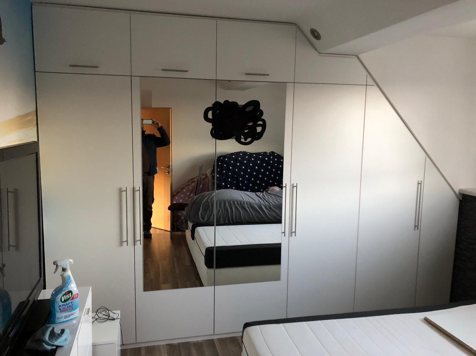 Eine Person fotografiert sich im Spiegel eines weißen Kleiderschranks im Schlafzimmer