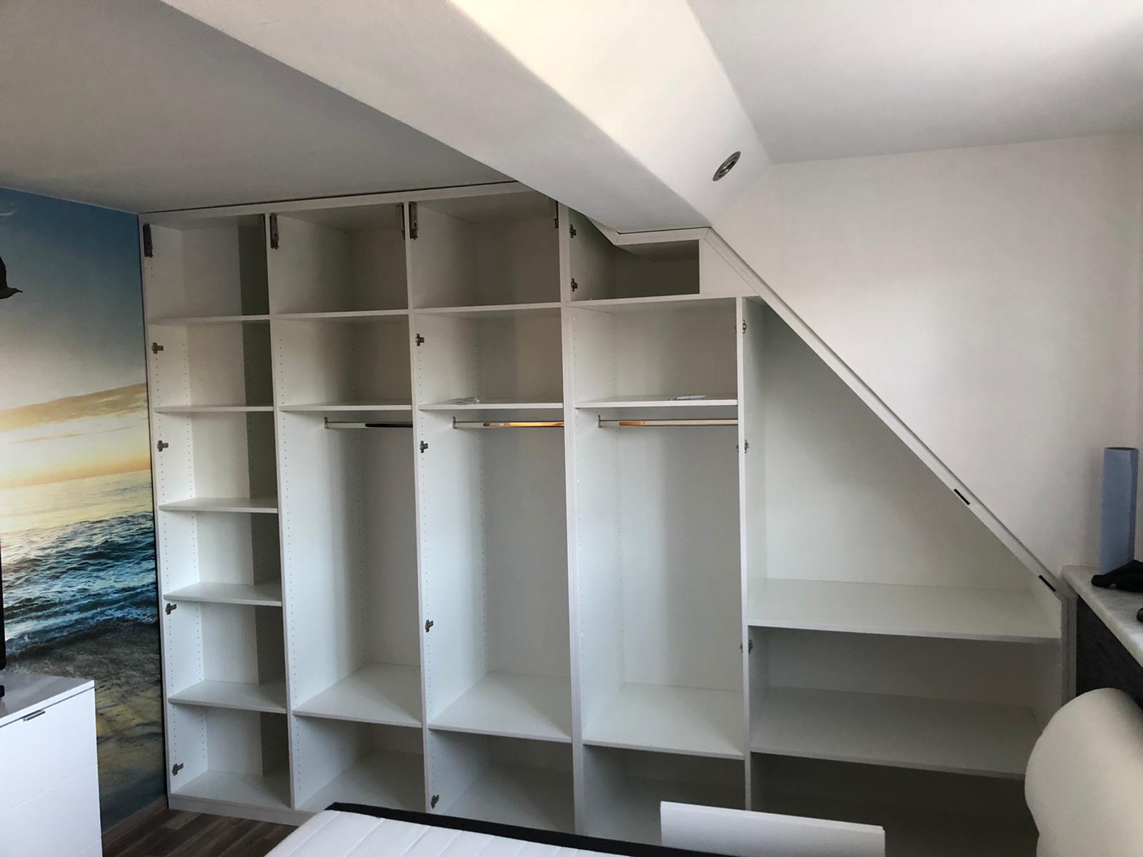 Ein weißer Einbauschrank mit Regalen und Kleiderstangen steht unter einer Dachschräge