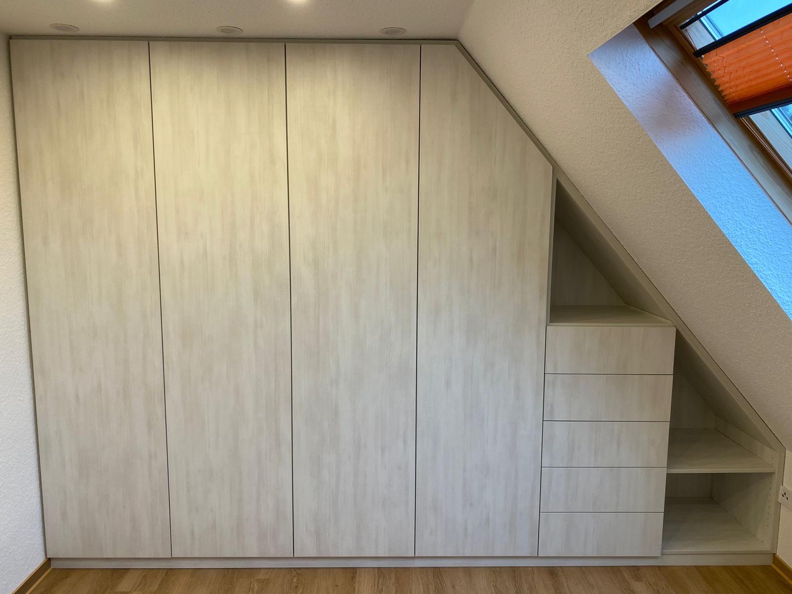 Ein maßgefertigter Einbauschrank aus hellem Holz mit schrägen Fächern und Schubladen