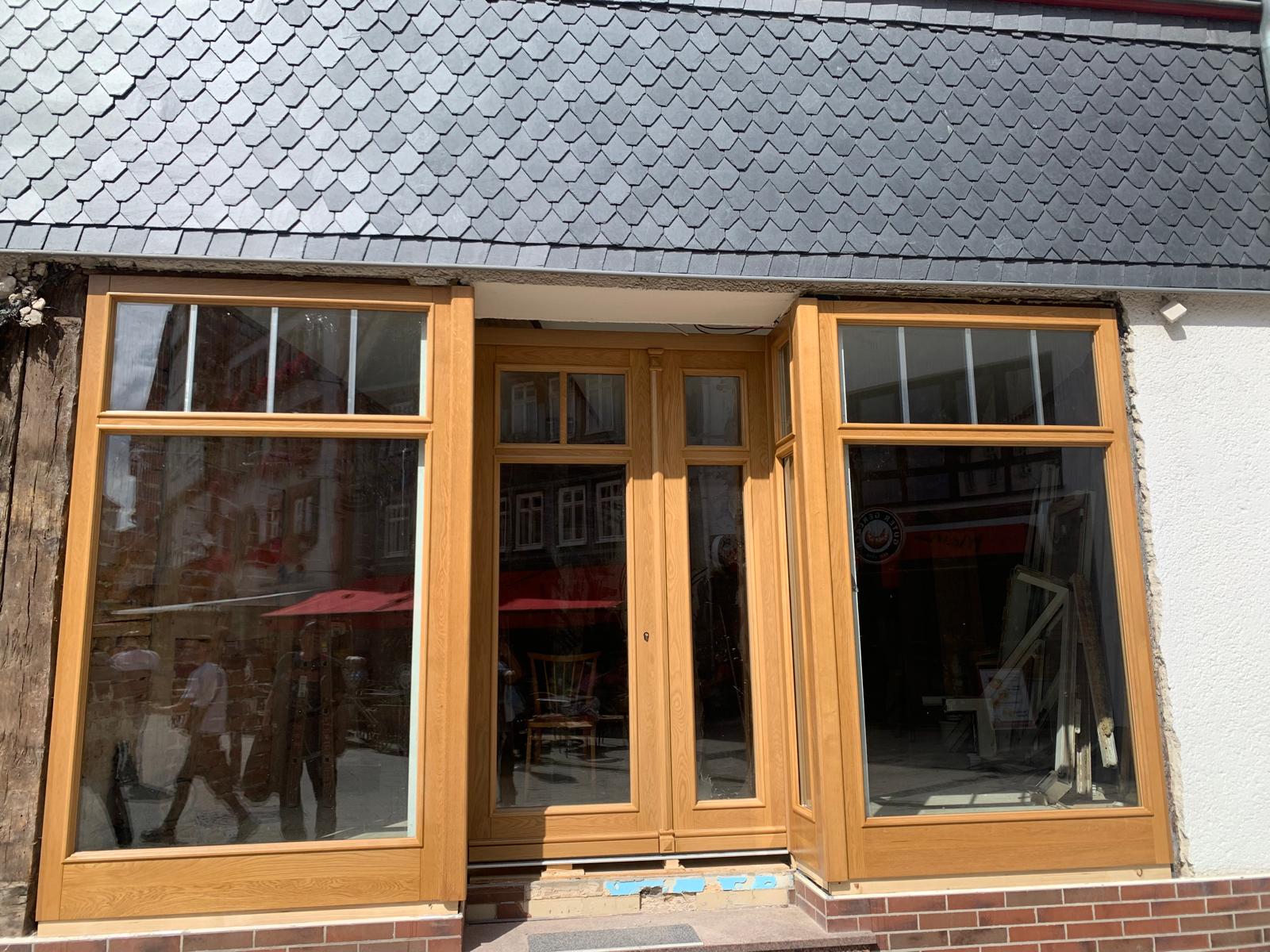 Zwei Personen mit neutralem Gesichtsausdruck spiegeln sich in einer großen Fensterfront