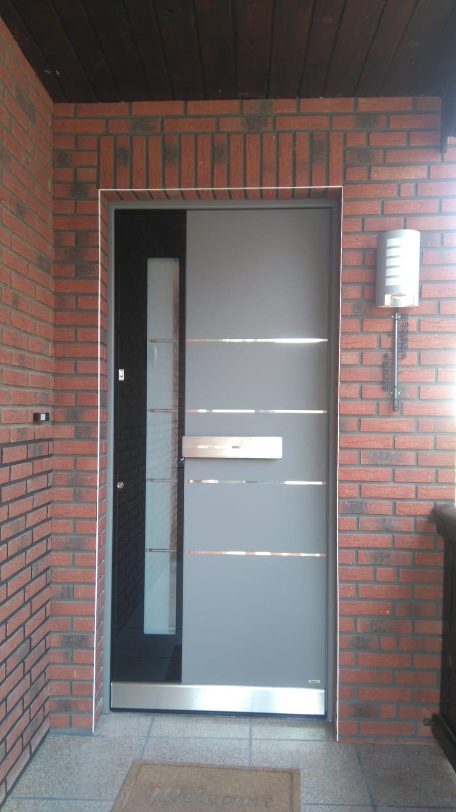 Graue moderne Tür mit horizontalen Metallstreifen in rotem Backsteinrahmen