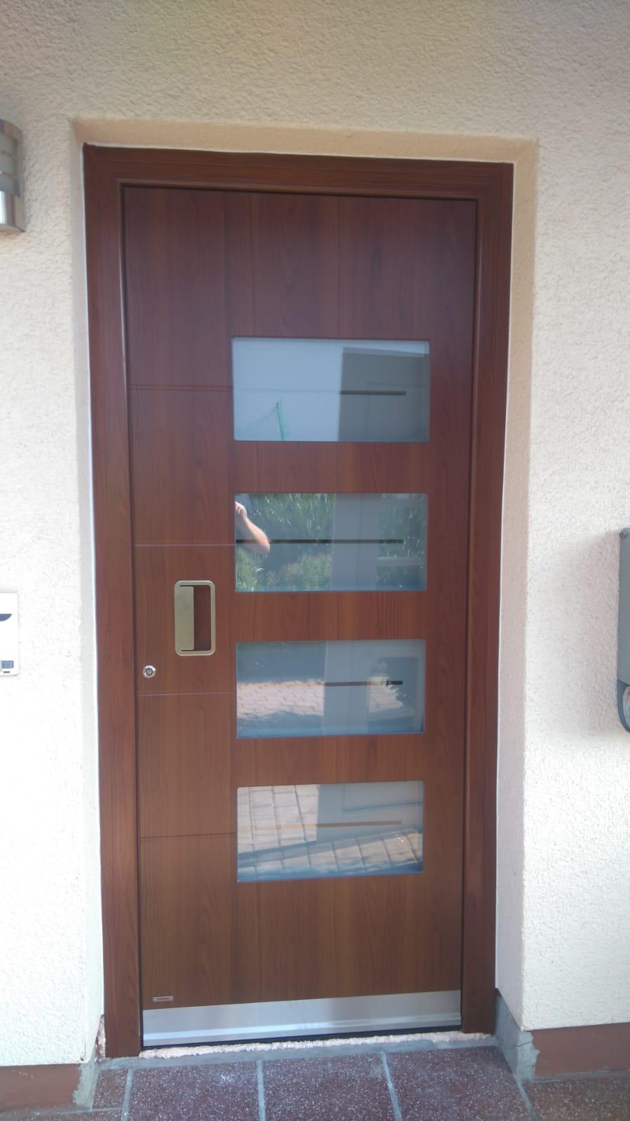 Eine braune Haustür mit vier rechteckigen Milchglasfenstern und silbernem Griff